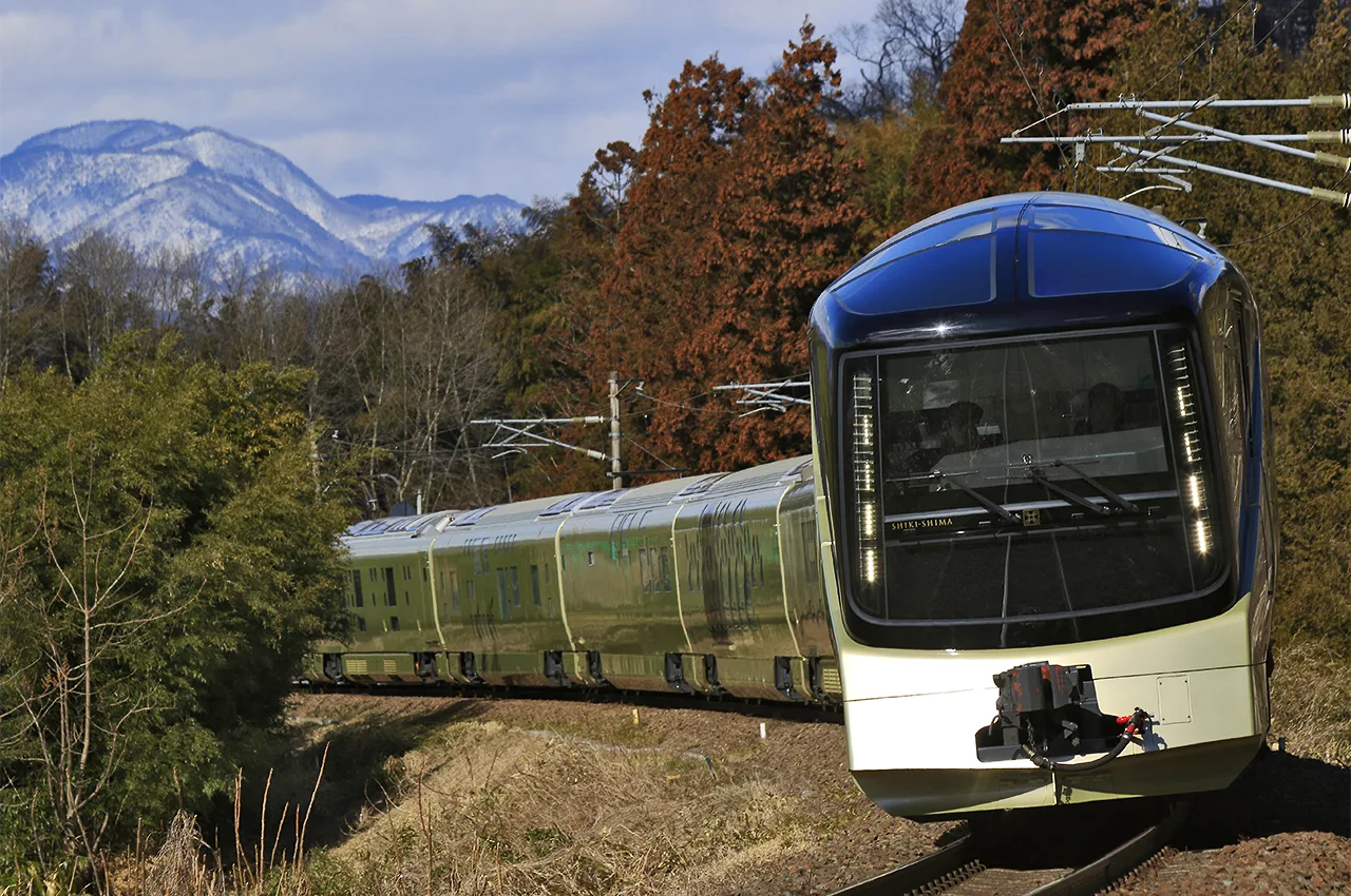 Tren de lujo Shiki-Shima de JR East circulando entre montañas nevadas y bosque otoñal en Japón